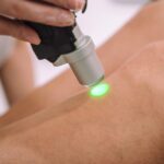 Close up shot of gloved hand with the laser hair removal machine's handpiece along woman's leg.