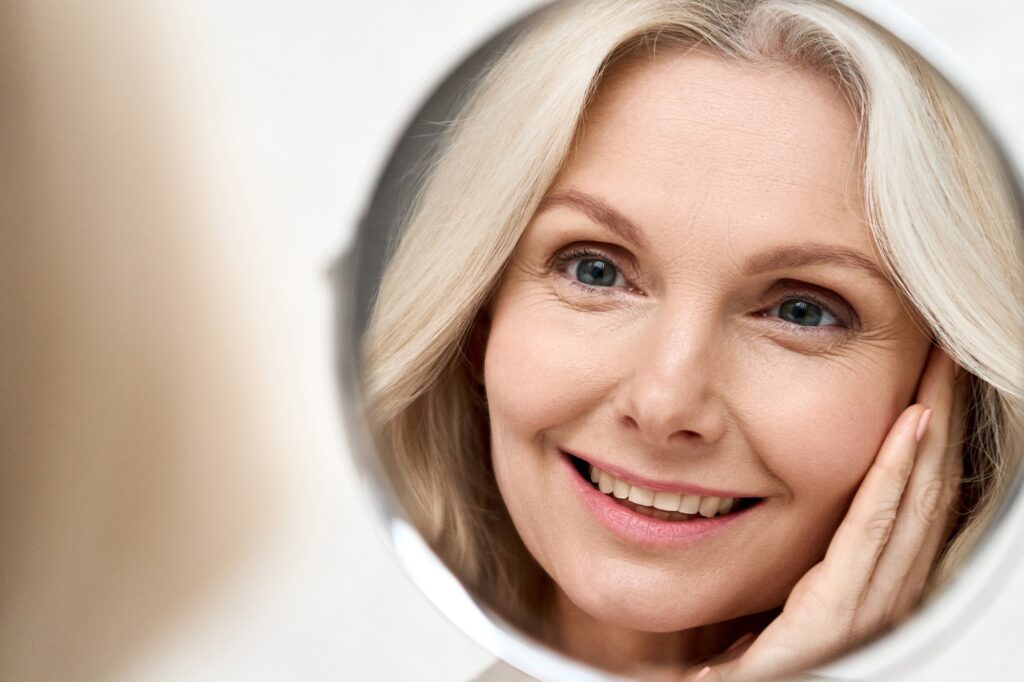 Happy middle aged woman looking at mirror. Antiaging beauty care concept.