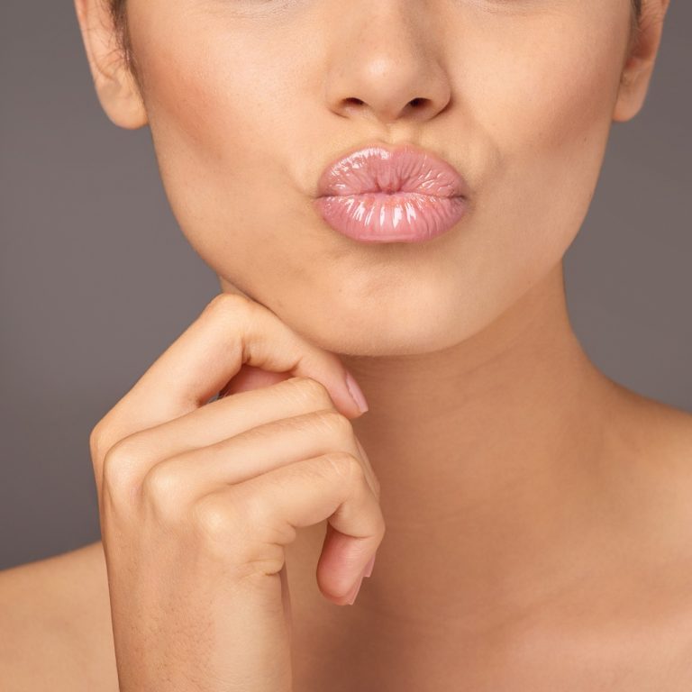Closeup studio shot of a woman with gorgeous glossy lips against a gray background