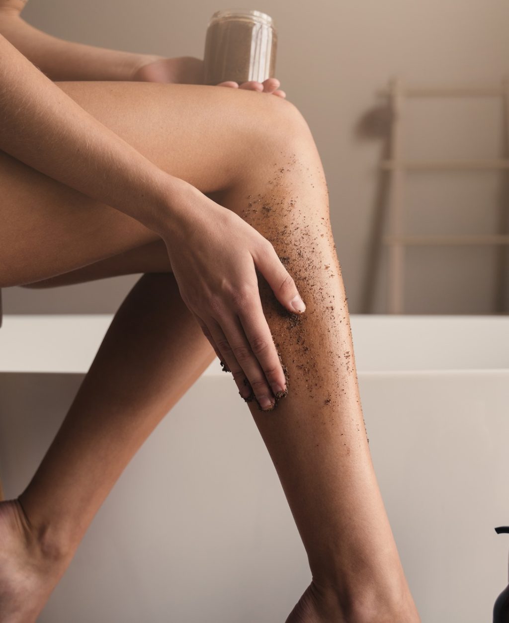 Cropped image of female hand applying peeling coffee scrub, massaging legs in bathroom