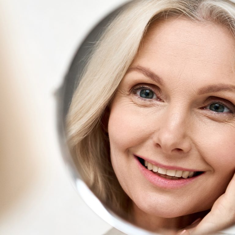 Happy mid aged woman looking at mirror. Antiaging beauty care concept.