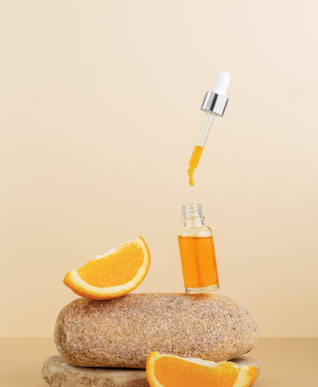 Serum vitamin C in cosmetic bottle, orange citrus slices on stone